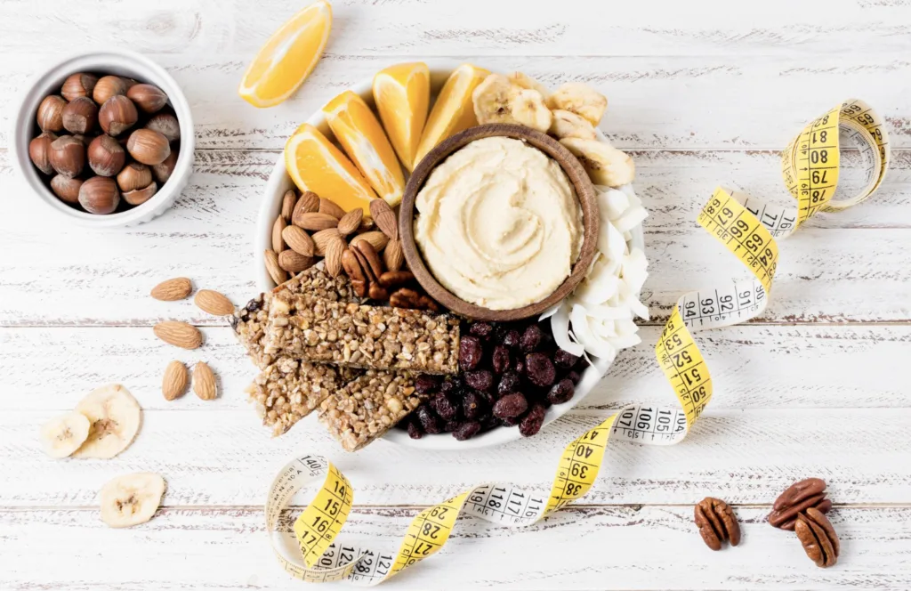 Fiber-rich foods for weight loss including hummus, nuts, fruit, and granola bars with a measuring tape