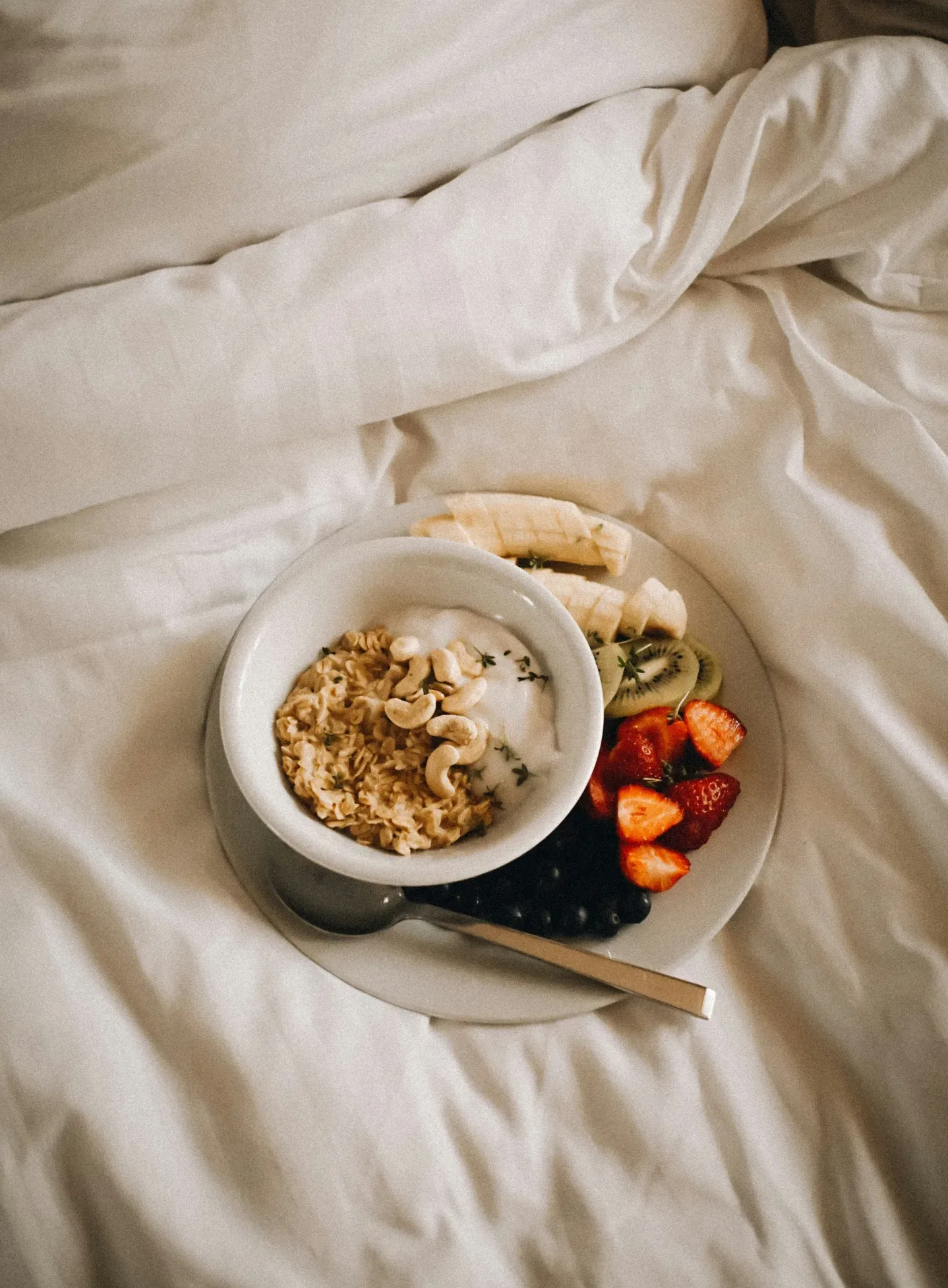 Oatmeal and a plate of fruit arranged on a bed