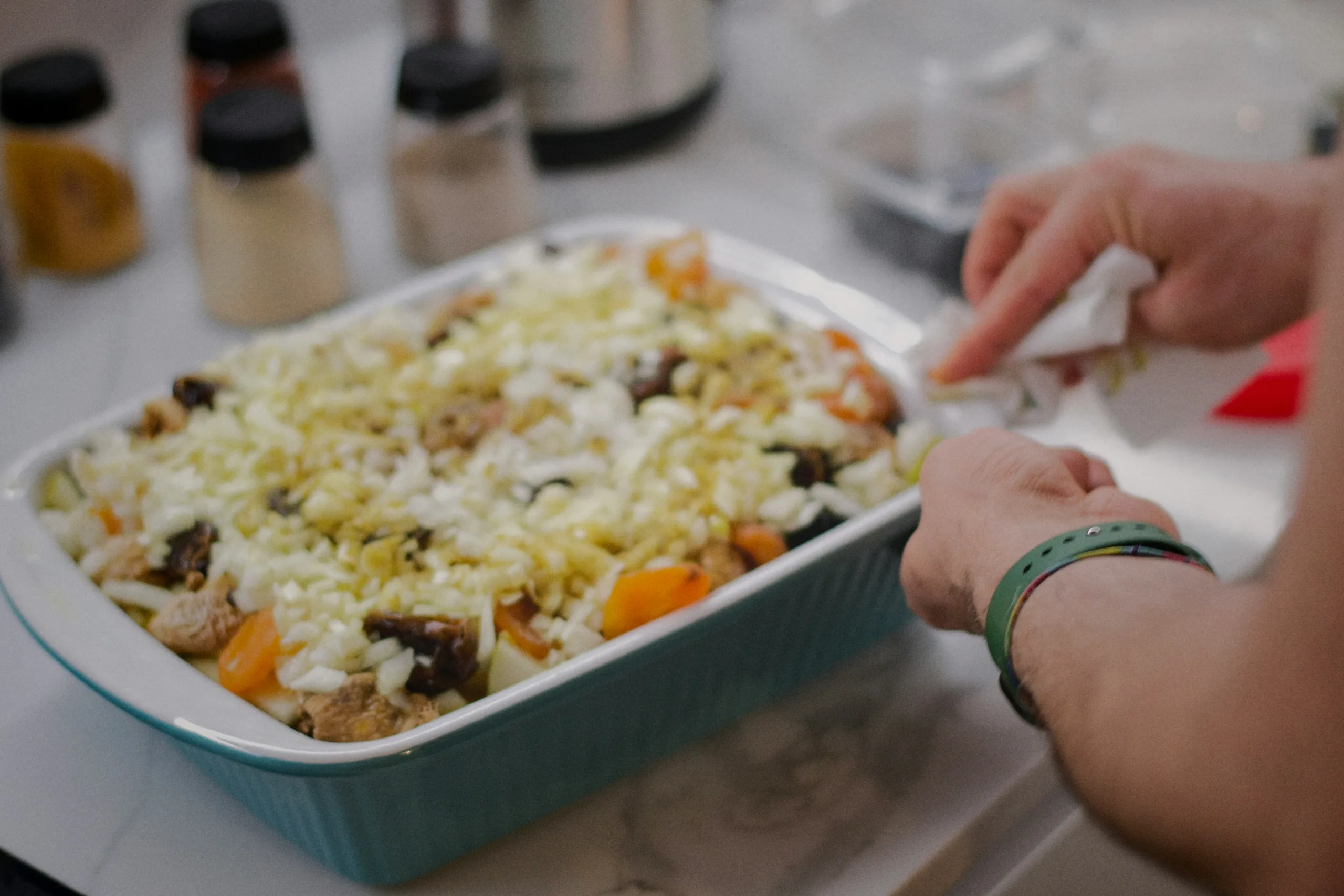 Hands adding chopped vegetables to a baking dish