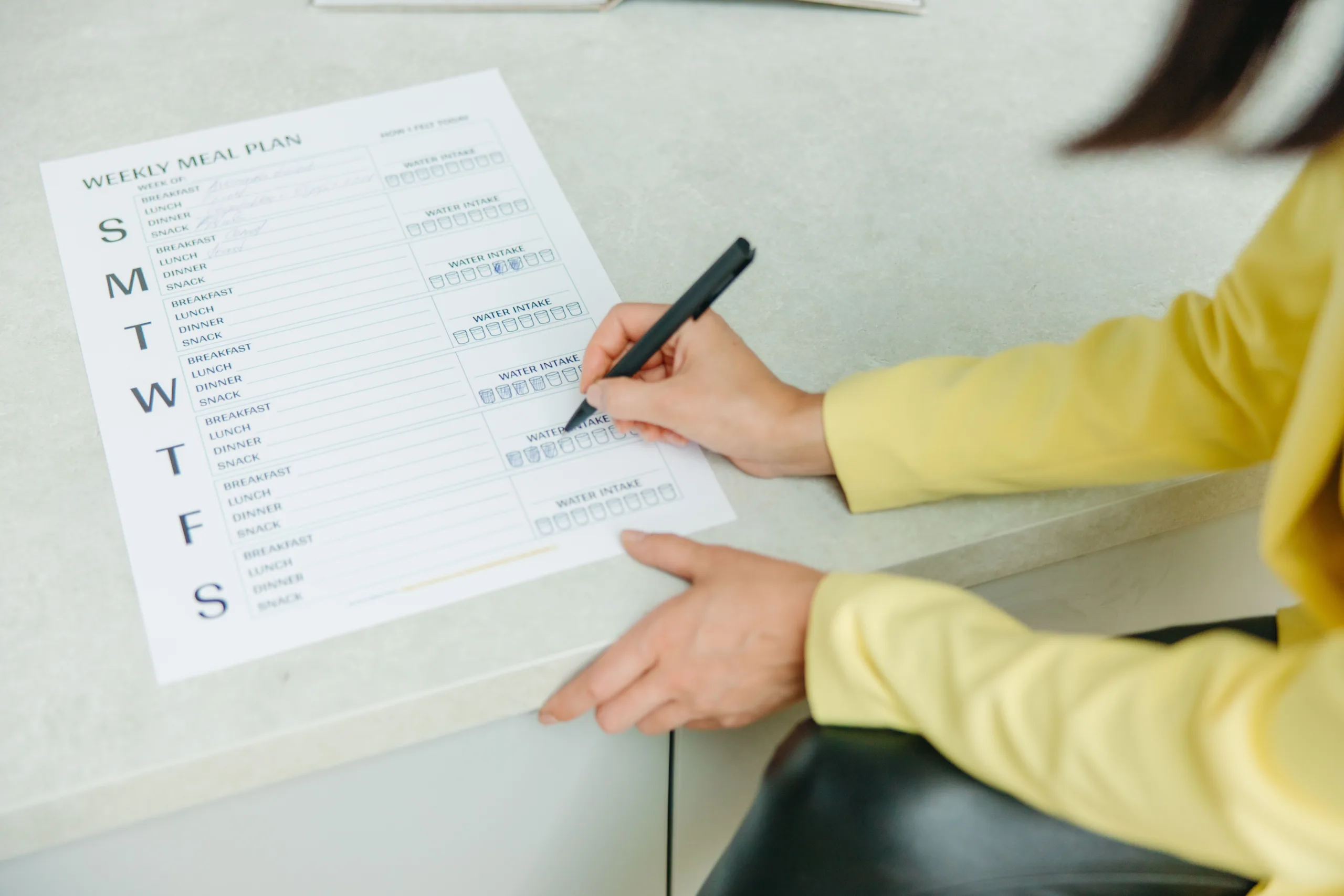 Hands completing a weekly meal planner with a pen