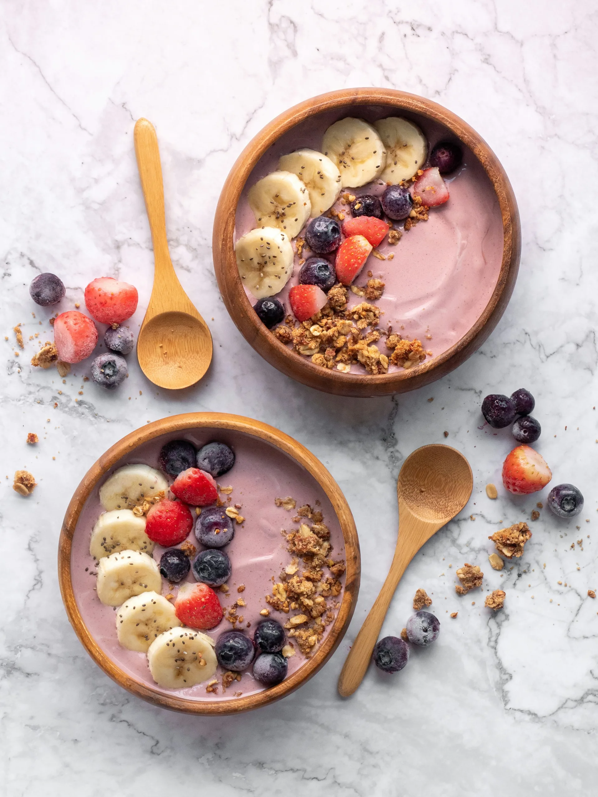 Two acai bowls topped with banana slices, berries and granola